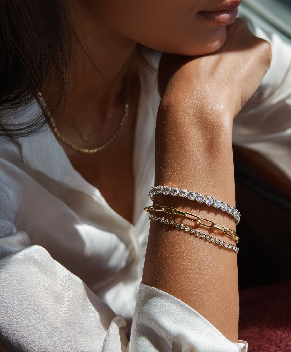 Diamond tennis bracelet layered with a gold chain on a woman's wrist, soft natural light
