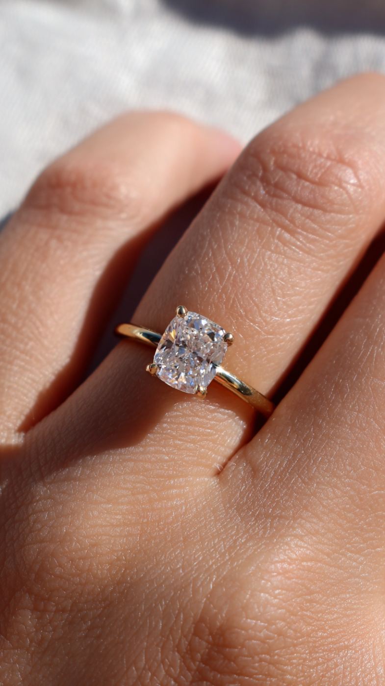 A cushion-cut diamond solitaire engagement ring on a finger